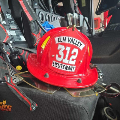 Red fire helmet with 'Elm Valley 312 Lieutenant' on a car seat
