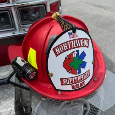 Red fire helmet with 'Northwood Safety Officer' emblem attached to a fire truck.
