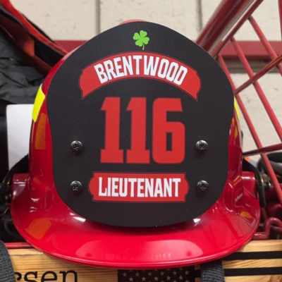 Red fire helmet with 'Brentwood 116 Lieutenant' label on a white tiled wall background