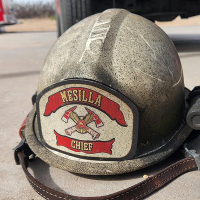 Vintage fire helmet with 'Mesilla Chief' patch on a pavement background