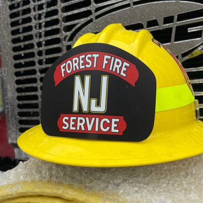 Yellow fire helmet with 'Forest Fire NJ Service' label on a fire truck background